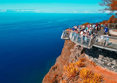 Tourists enjoying the breathtaking view from Cabo Girão Skywalk, a glass-floored platform perched on a dramatic cliff overlooking the Atlantic Ocean in Madeira
