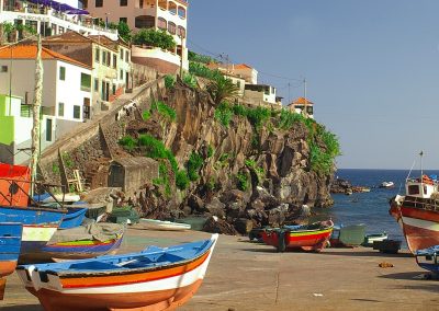 Colorful fishing boats resting on the shore of Câmara de Lobos, a picturesque fishing village in Madeira, with cliffside houses and the Atlantic Ocean in the background